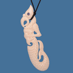 Carved bone manai pendant with a paua eye on a blue background