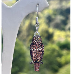 Morepork earring on a white stand with a blurred green background