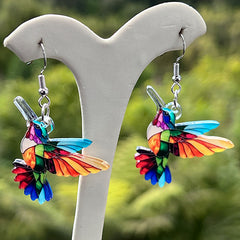 Colorful hummingbird-shaped earrings on a white stand with a blurred green background